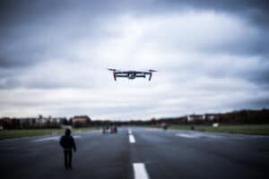 a man walking down the road with a remote controlled airplane flying overhead